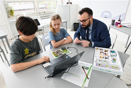 Kinder und Lehrkraft mit Laptop am Tisch sitzend