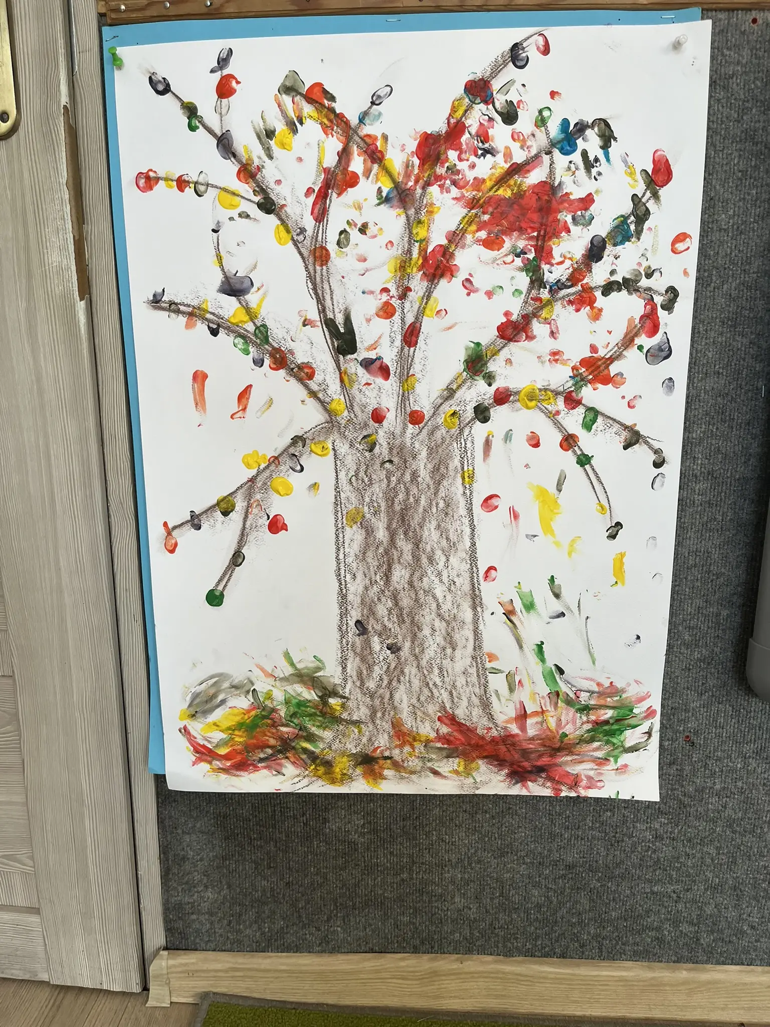 Ein gemalter Baum auf einem großen Blatt erhält bunte Blätter aus Fingerfarben