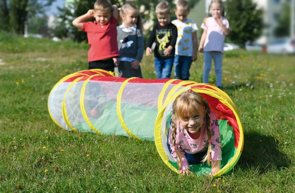 Einsatz von Sportgeräten im Freien: Kinder krabbeln auf der Wiese durch einen Spieltunnel