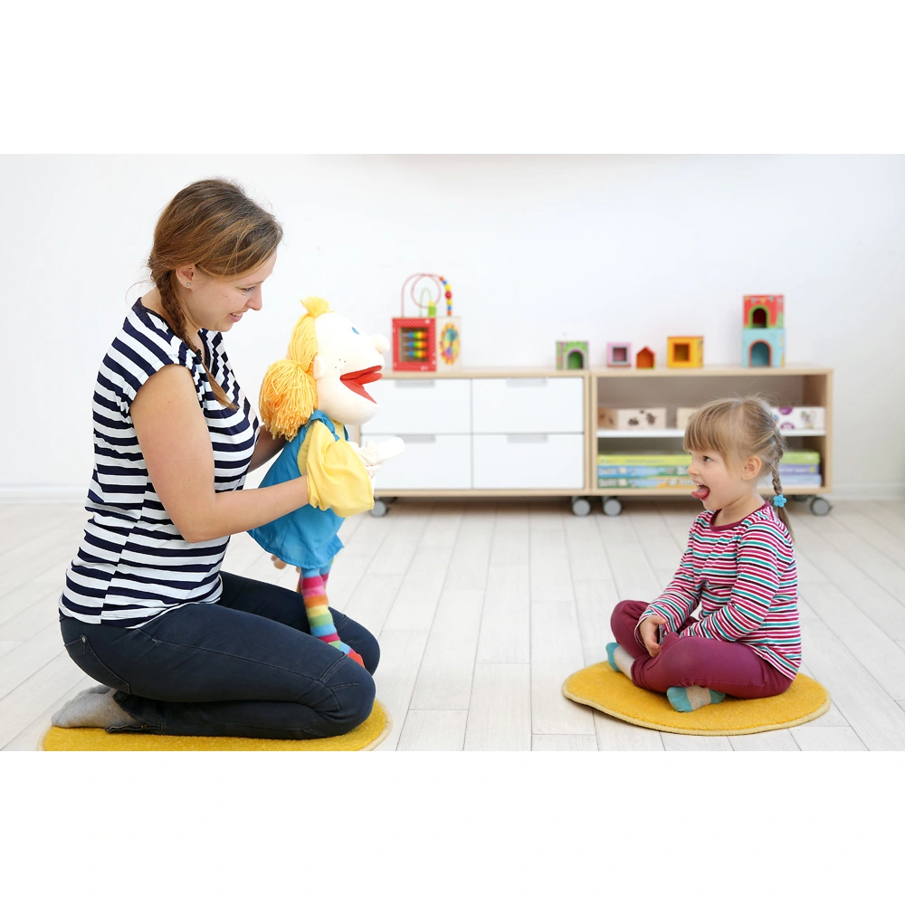 Ein Logopäde zeigt einem Kind über eine Handpuppe Mund- und Zungenbewegungen