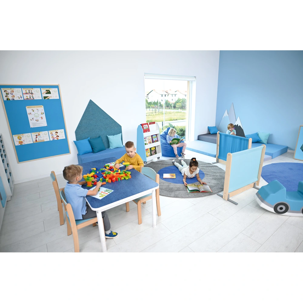 Kinder spielen und lesen in einem blau gestalteten Raum mit Tischgruppe, Lümmelecke und Spielteppich.