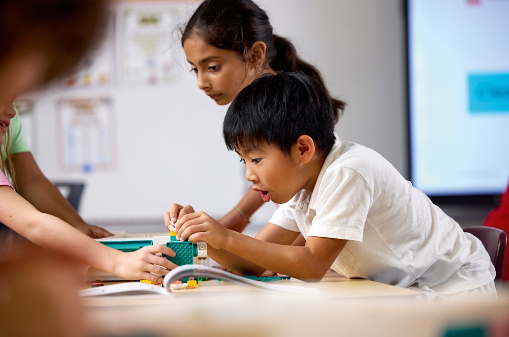 Zwei Kinder konzentrieren sich auf den Bau eines LEGO-Modells im Klassenzimmer.