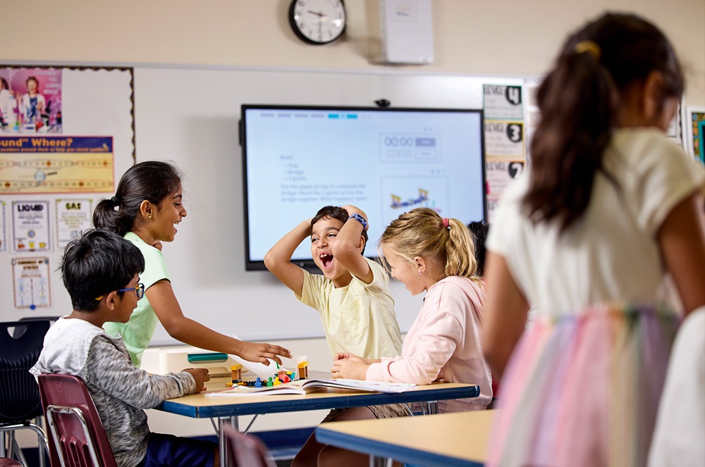Eine Gruppe von Grundschulkindern arbeitet gemeinsam an einem LEGO Education Projekt und lacht im Klassenzimmer.