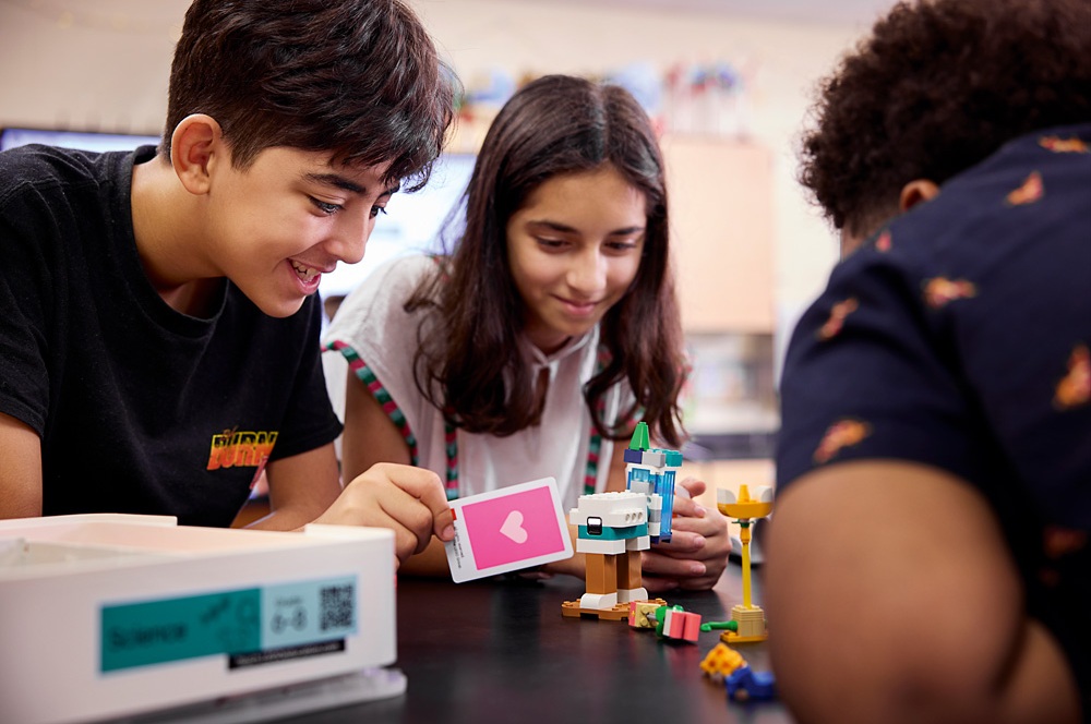 Jugendliche bauen gemeinsam ein LEGO® Education Modell und zeigen eine rosa Karte mit Herzsymbol.