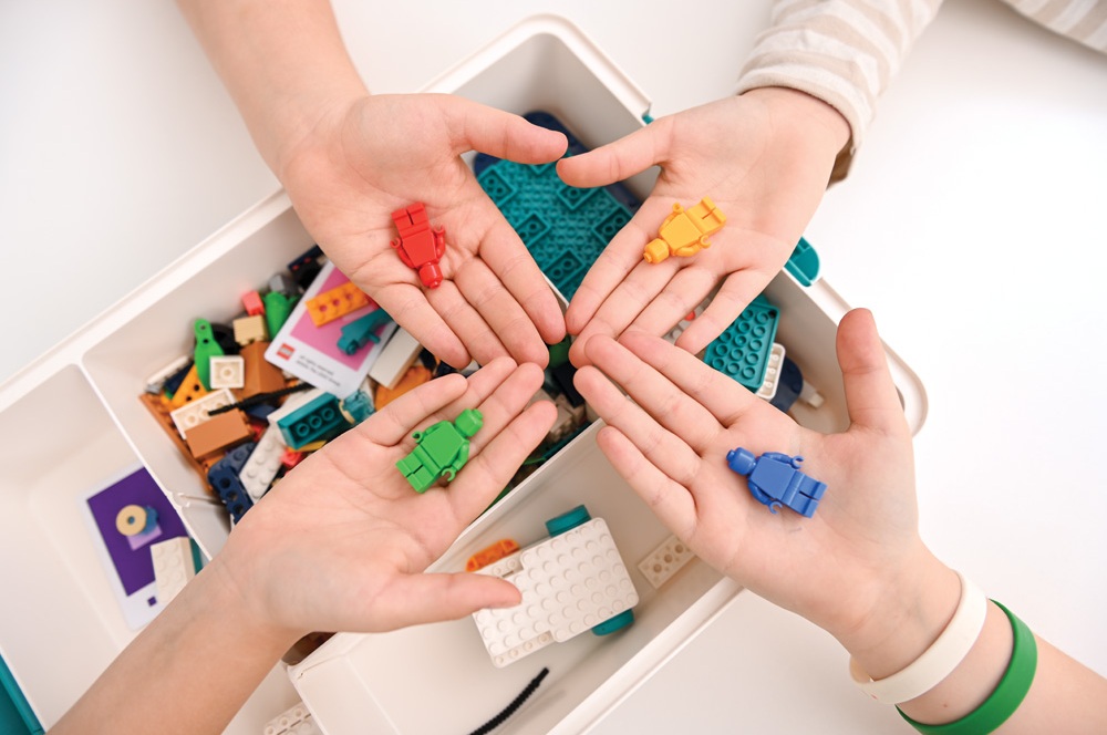 Vier Kinder zeigen farbige LEGO® Figuren in den Händen über einem offenen LEGO® Kasten.